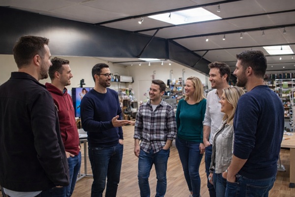 Les collaborateurs échangent entre eux en étant debout dans le showroom de leur agence de communication car ils ont aimé la formation de MOOVENCE